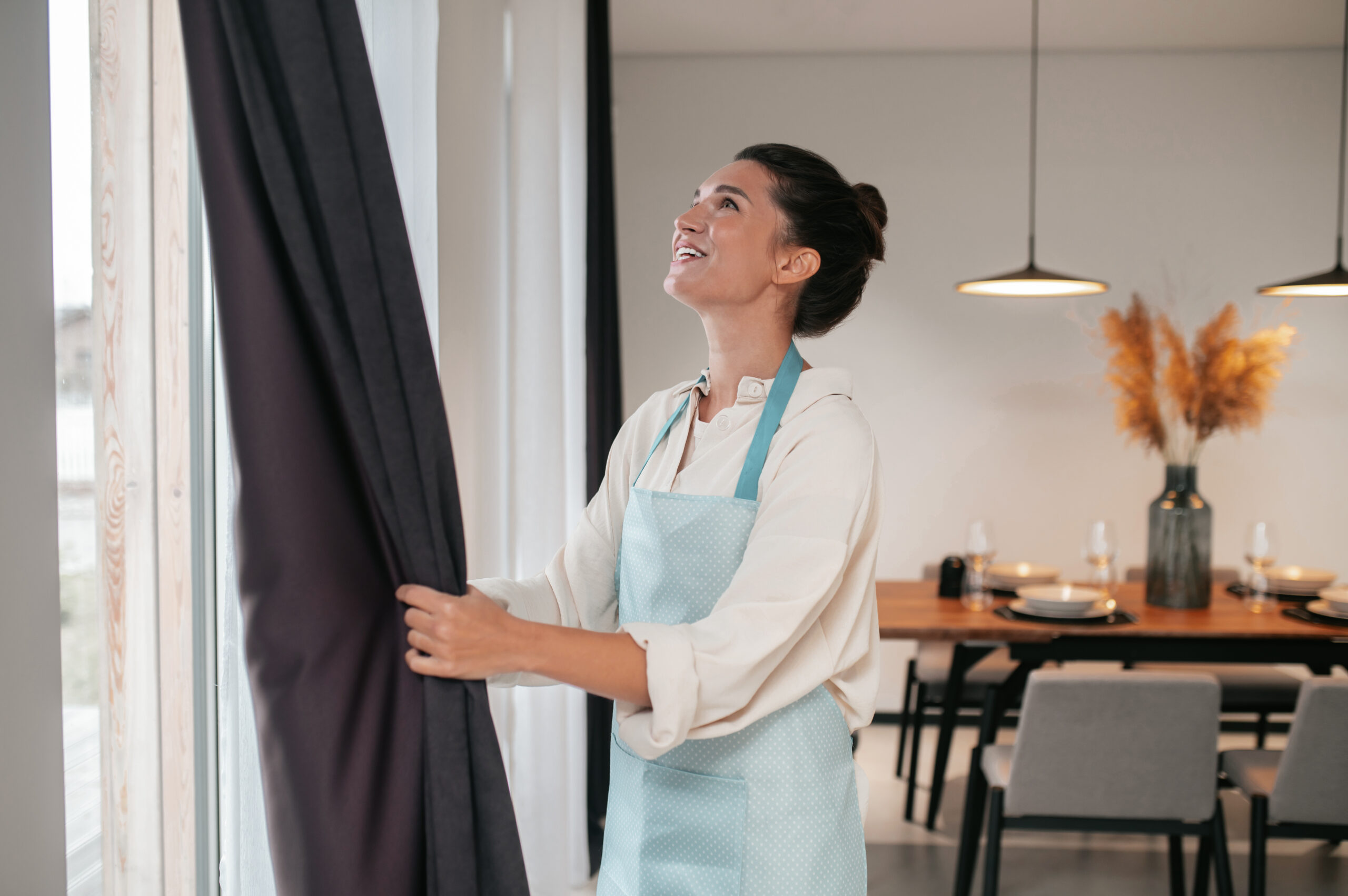 young woman standing near the widnow and fixing the curtains